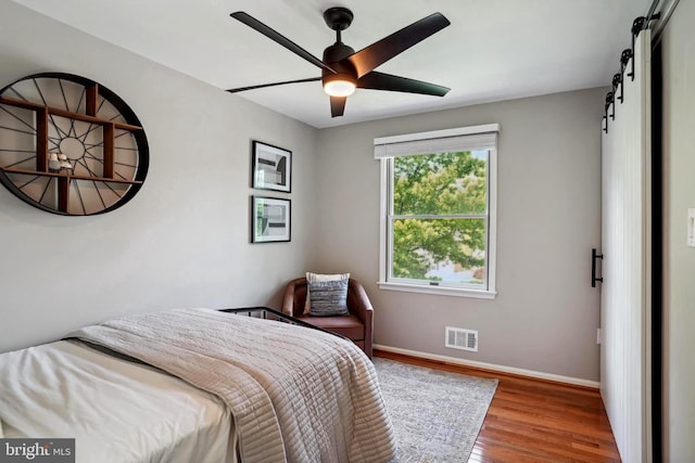 bedroom with a barn door, a ceiling fan, baseboards, wood finished floors, and visible vents