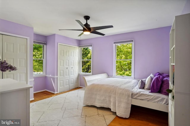bedroom with two closets, ceiling fan, baseboards, and light wood finished floors