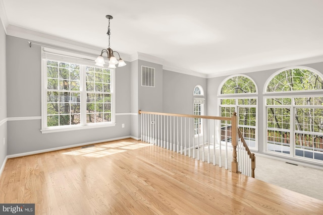 empty room with baseboards, ornamental molding, a chandelier, and visible vents
