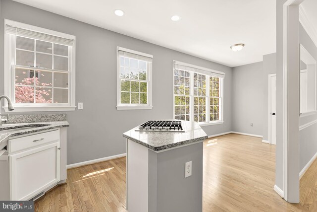 kitchen featuring stainless steel gas stovetop, light stone counters, a sink, light wood-style floors, and white cabinetry