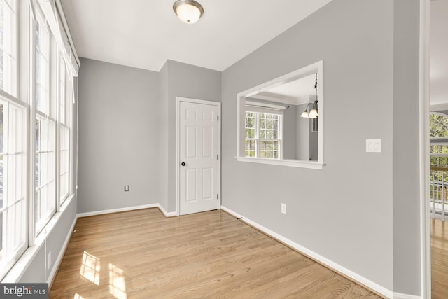 empty room featuring a chandelier, light wood finished floors, and baseboards