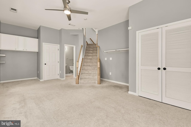 interior space with stairway, visible vents, a ceiling fan, baseboards, and light colored carpet