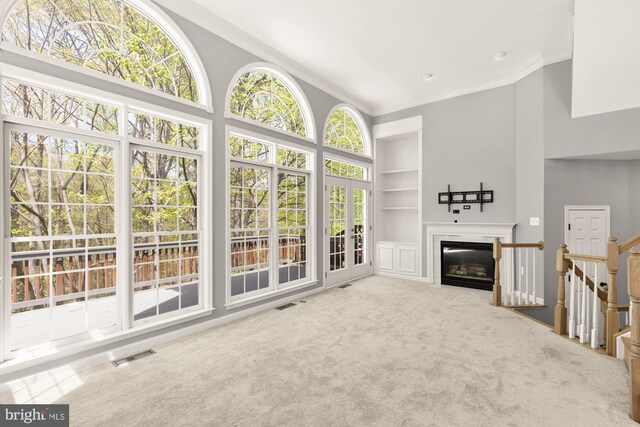 unfurnished living room featuring a glass covered fireplace, built in shelves, ornamental molding, carpet flooring, and visible vents