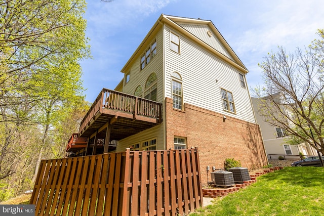 back of property with central AC unit, fence, brick siding, a wooden deck, and a lawn