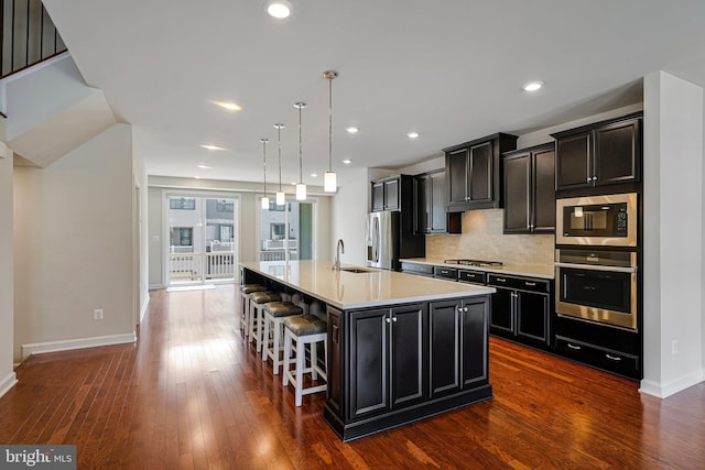 kitchen with dark cabinets, a kitchen bar, light countertops, appliances with stainless steel finishes, and a spacious island