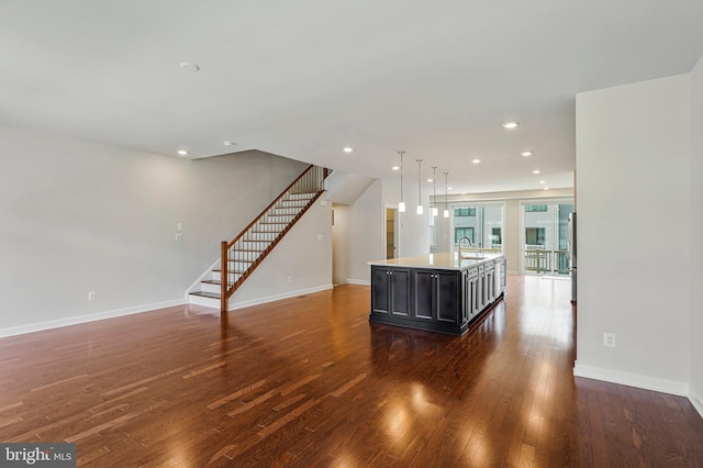 kitchen featuring baseboards, a sink, wood finished floors, light countertops, and an island with sink