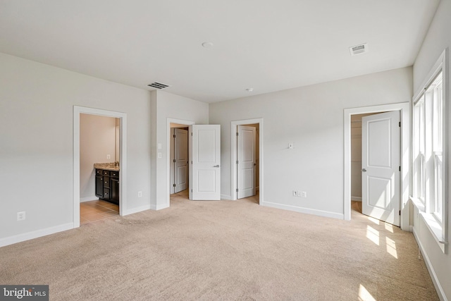 unfurnished bedroom featuring a walk in closet, light carpet, baseboards, and visible vents