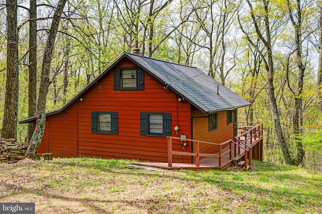 view of side of home with a deck, a view of trees, and roof with shingles