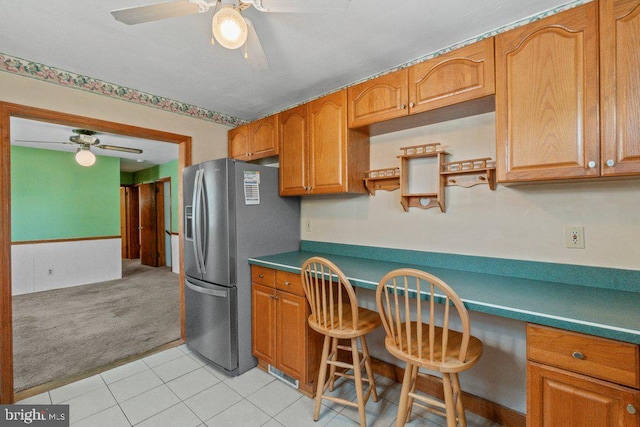 kitchen featuring ceiling fan, stainless steel fridge, brown cabinetry, and built in study area