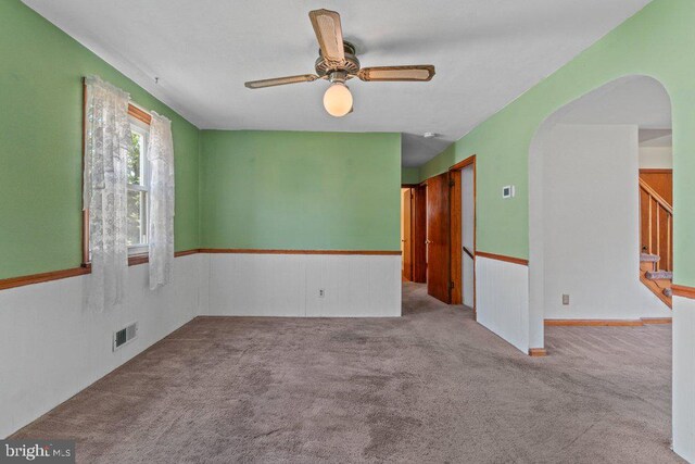 carpeted spare room featuring visible vents, arched walkways, a ceiling fan, and stairway