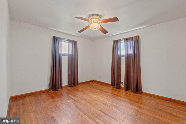 empty room featuring baseboards, a ceiling fan, light wood-style flooring, and a wealth of natural light