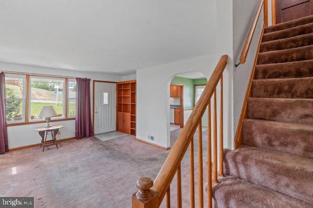 foyer featuring light carpet, arched walkways, baseboards, visible vents, and stairway