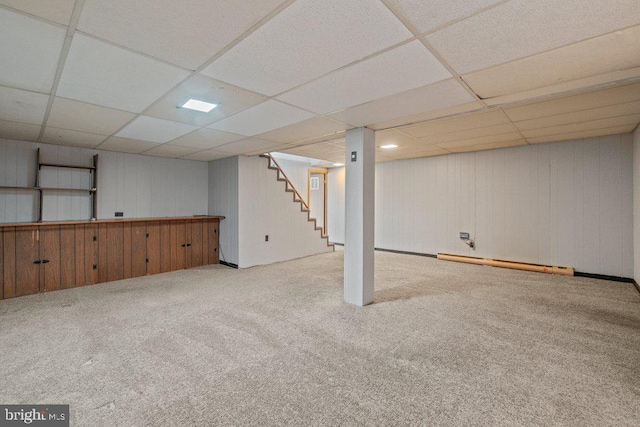 finished below grade area featuring stairs, a paneled ceiling, carpet, and a baseboard radiator