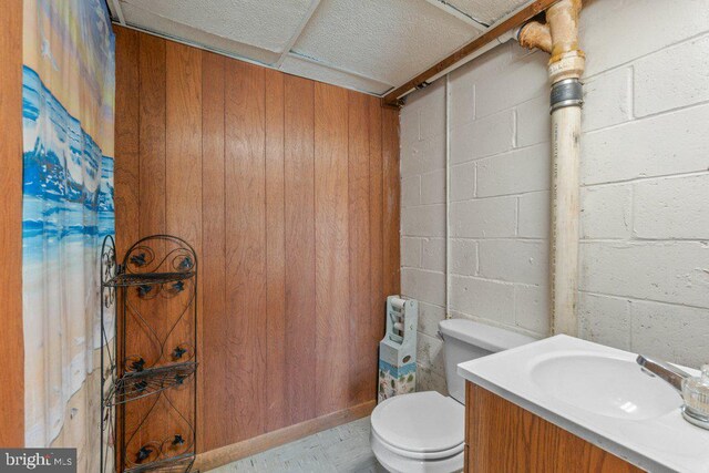 half bath with concrete block wall, vanity, and toilet