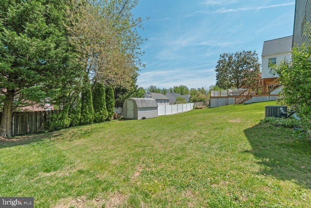 view of yard with an outdoor structure, a wooden deck, a fenced backyard, central AC unit, and a storage shed