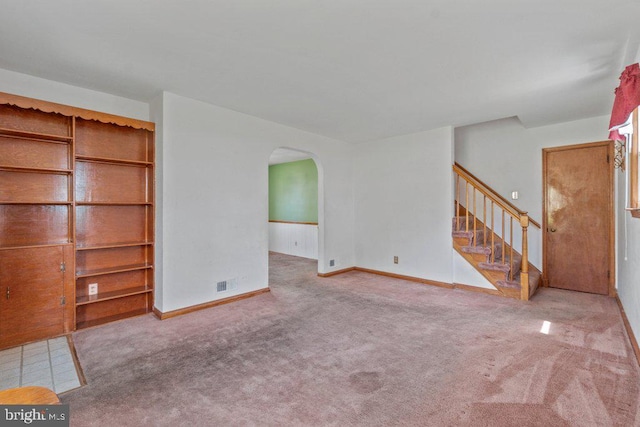 unfurnished living room featuring visible vents, arched walkways, carpet, and stairway