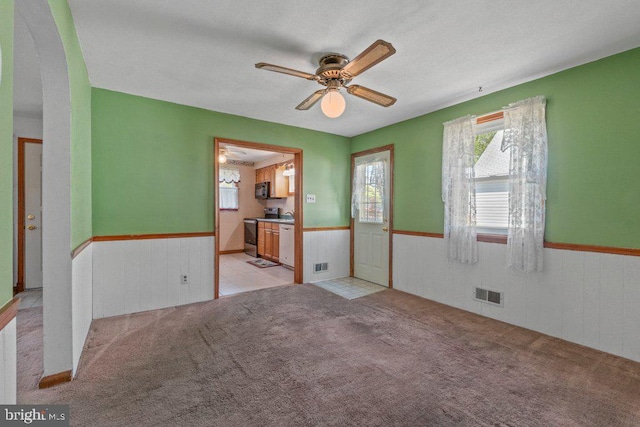 unfurnished room featuring visible vents, ceiling fan, and a wainscoted wall