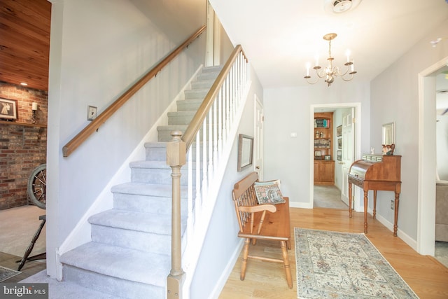 1701 Holicong Rd, New Hope, PA 18938 - stairway featuring brick wall, baseboards, wood finished floors, and a notable chandelier