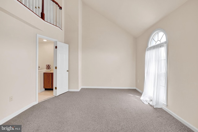 spare room with high vaulted ceiling, carpet flooring, and baseboards