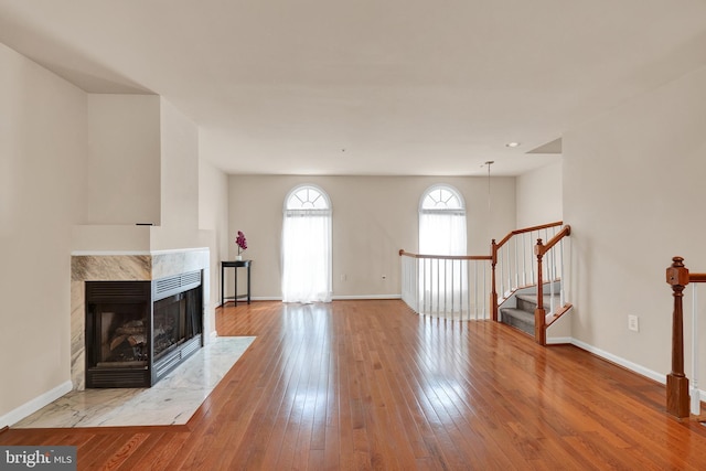 unfurnished living room featuring wood-type flooring, baseboards, stairway, and a fireplace