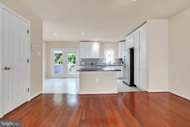 kitchen with stainless steel refrigerator with ice dispenser, white cabinetry, a kitchen island, and light wood finished floors