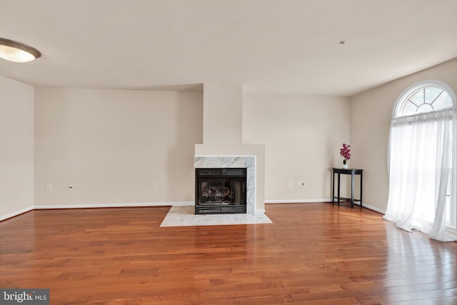 unfurnished living room featuring baseboards, wood finished floors, and a high end fireplace