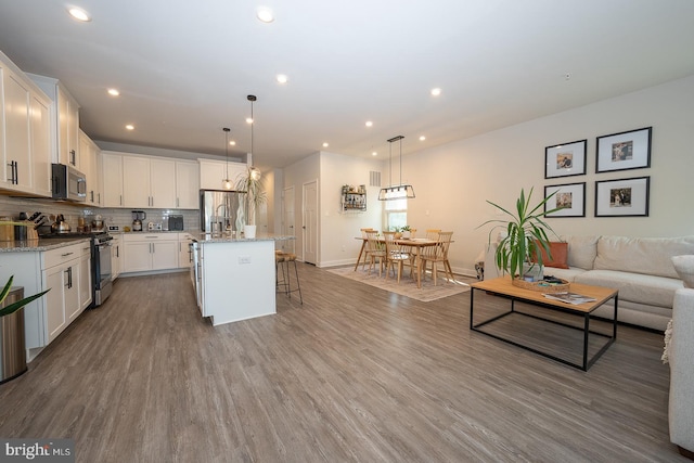 kitchen with a breakfast bar area, stainless steel appliances, white cabinetry, wood finished floors, and tasteful backsplash