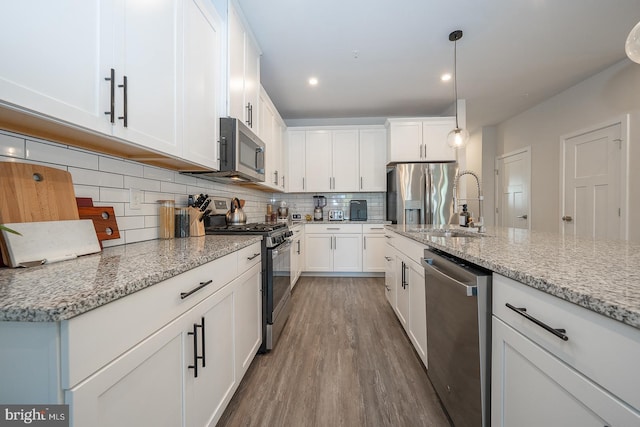 kitchen with a sink, appliances with stainless steel finishes, wood finished floors, and white cabinets