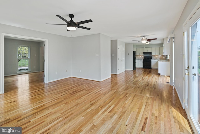 unfurnished living room with light wood-type flooring, a ceiling fan, a sink, and baseboards