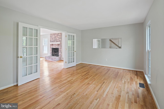 empty room featuring french doors, visible vents, a brick fireplace, wood finished floors, and baseboards