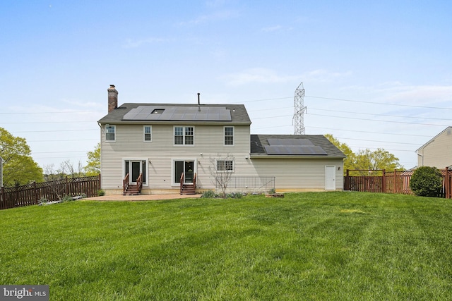 back of property featuring a chimney, a fenced backyard, roof mounted solar panels, a yard, and entry steps