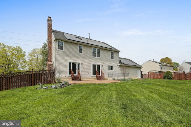 back of house with a yard, solar panels, entry steps, and a chimney