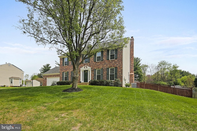 colonial inspired home featuring fence, a chimney, a front yard, and brick siding