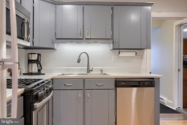 kitchen featuring gray cabinets, a baseboard heating unit, appliances with stainless steel finishes, light countertops, and a sink