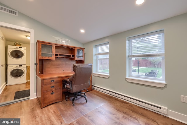 office space with visible vents, a baseboard heating unit, light wood-type flooring, stacked washer and clothes dryer, and lofted ceiling