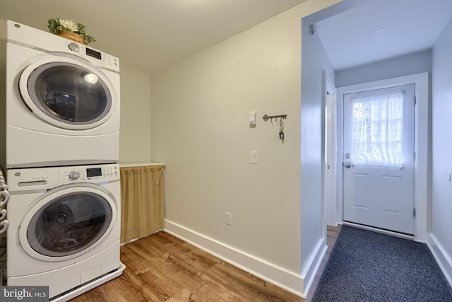 laundry room with baseboards, wood finished floors, stacked washer and dryer, and laundry area