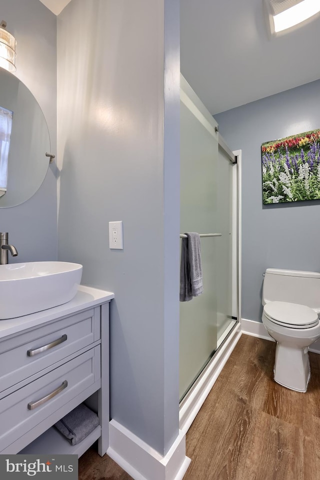 bathroom featuring wood finished floors, toilet, vanity, baseboards, and a stall shower
