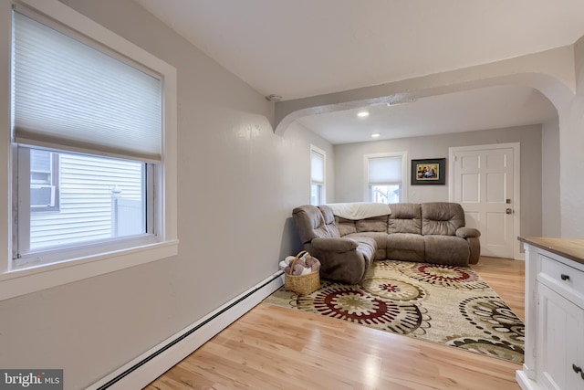 living area featuring arched walkways, baseboard heating, and light wood-style flooring