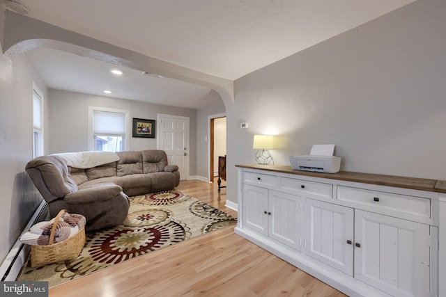 living area with recessed lighting, arched walkways, a baseboard heating unit, light wood-style floors, and baseboards