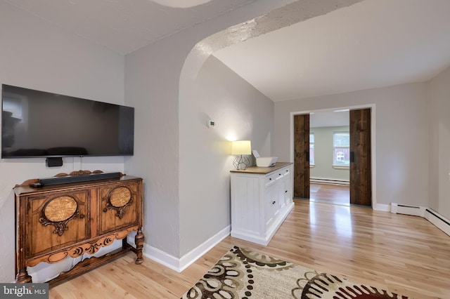 interior space featuring light wood finished floors, baseboards, arched walkways, baseboard heating, and a baseboard radiator