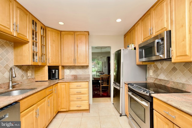 kitchen with a sink, stainless steel appliances, light tile patterned floors, backsplash, and light stone counters