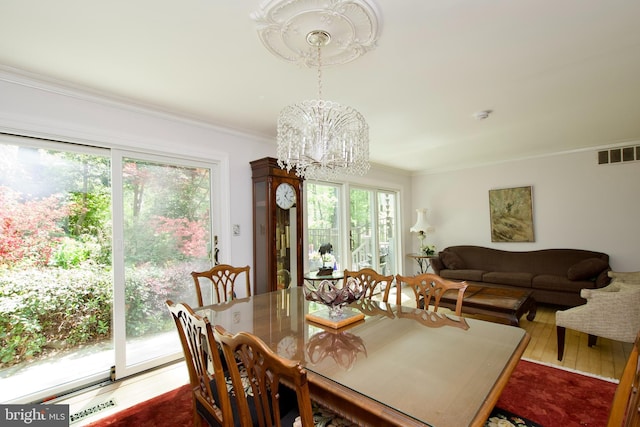 dining area featuring a chandelier, visible vents, ornamental molding, and wood finished floors