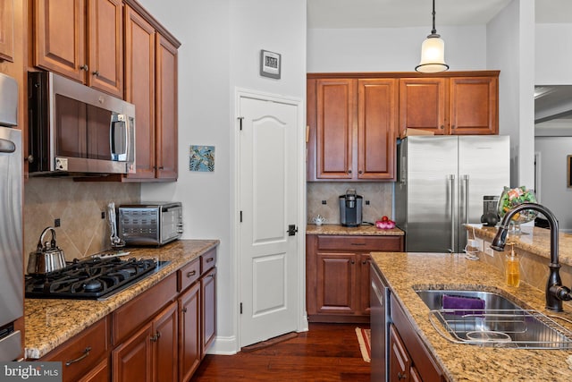 kitchen featuring light stone countertops, dark wood-style floors, tasteful backsplash, a sink, and appliances with stainless steel finishes