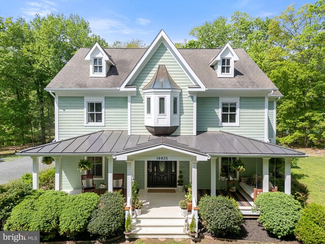 view of front facade featuring roof with shingles, covered porch, and a standing seam roof