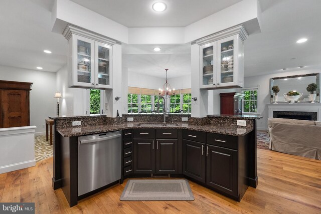 kitchen with light wood-type flooring, dishwasher, a sink, an inviting chandelier, and dark stone counters