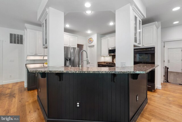 kitchen with a kitchen bar, dark stone countertops, light wood finished floors, stainless steel appliances, and white cabinetry