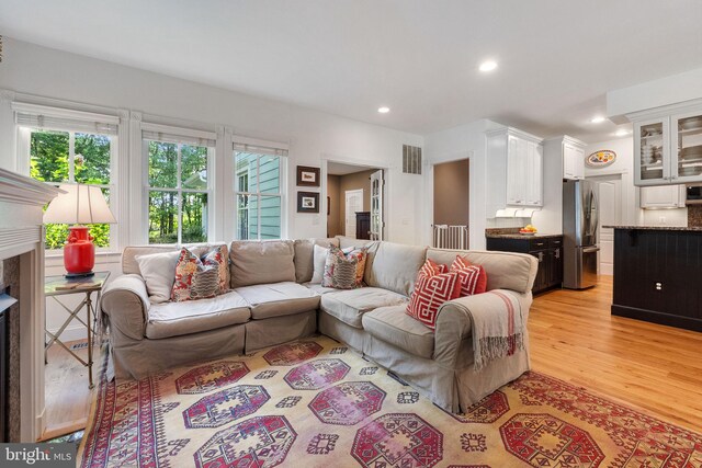 living room with recessed lighting, visible vents, a high end fireplace, and light wood-type flooring