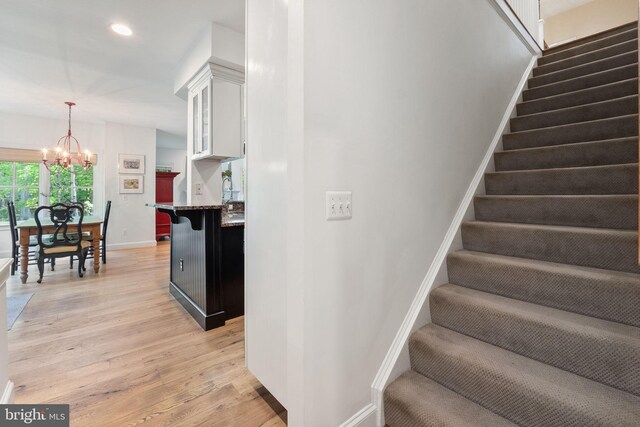 stairway featuring baseboards, recessed lighting, wood finished floors, and a chandelier