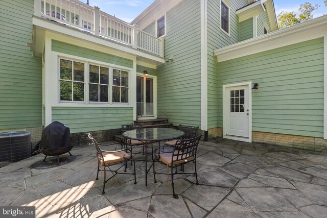 view of patio with a balcony, a grill, entry steps, central air condition unit, and outdoor dining space
