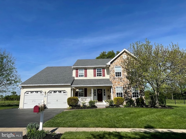 view of front of home featuring driveway, covered porch, an attached garage, stone siding, and a front lawn